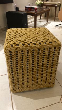 a yellow crocheted stool sitting on top of a white tile floor next to a wooden table