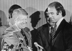 black and white photograph of two men shaking hands with microphones in front of them