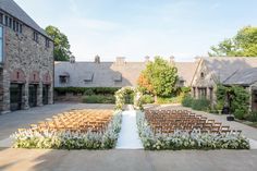 an outdoor ceremony set up with chairs and flowers on the aisle, in front of a stone building