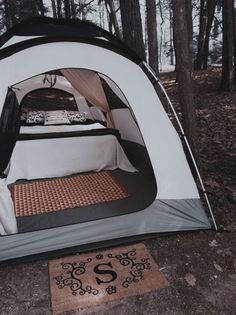 a tent set up in the woods with a door mat on the ground next to it