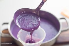 a spoon full of purple liquid being poured into a cup