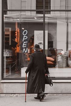 an old man walking down the street in front of a store window with his cane