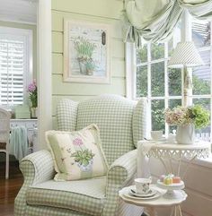 a green chair sitting in front of a window next to a table with flowers on it