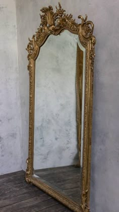 an ornate gold framed mirror sitting on top of a wooden floor next to a wall