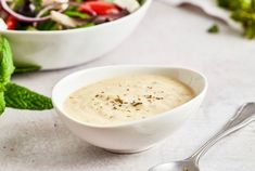 a white bowl filled with soup next to a salad on top of a tablecloth