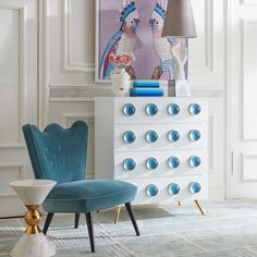 a blue chair sitting next to a white dresser with two lamps on top of it