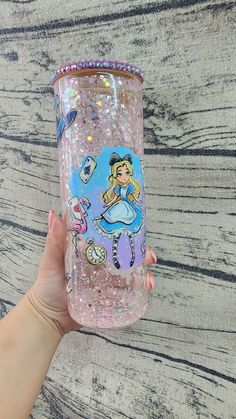 a hand holding a pink glittered tumbler with an image of a princess on it