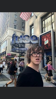 a man with glasses standing in front of a theater on a busy city street next to tall buildings