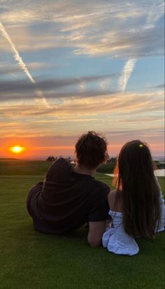 two people sitting on the grass watching the sun set