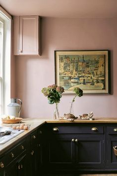 a painting hanging on the wall above a kitchen counter with flowers in vases and other items