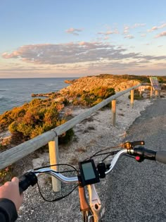 a person riding a bike down a road next to the ocean with a wooden fence