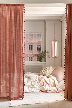 a bedroom with pink curtains and a bed covered in white sheets, pillows and blankets