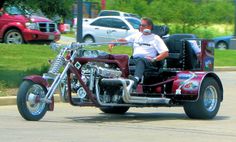 a man riding on the back of a red motorcycle down a street next to parked cars