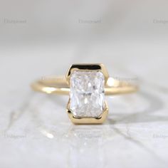 an engagement ring with a square cut diamond in the center on a white marble surface