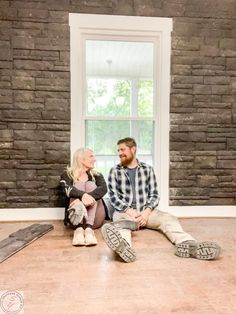 a man and woman sitting on the floor in front of a brick wall looking at each other