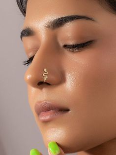 a close up of a woman with a nose ring on her nose and green nail polish