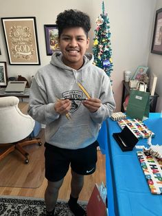 a young man standing in front of a table holding a pair of chopsticks