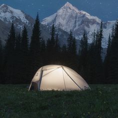 a tent is set up in the grass with mountains in the background at night time