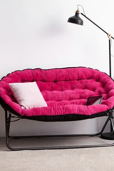 a pink futon sofa with a black frame and white pillow on the bottom, in front of a floor lamp