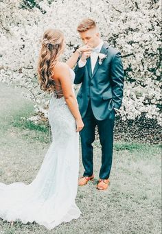 the bride and groom are standing in front of some trees with white flowers on it