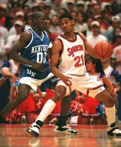 two basketball players in action on the court with people watching from the stands behind them