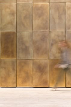 a blurry photo of a person walking past a wall with brown tiles on it