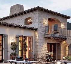 an outdoor dining area in front of a stone building with potted plants on the balcony