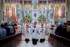 two men in white robes walking down the aisle of a church with other people behind them