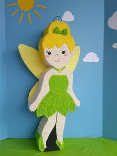 a paper doll with a green dress and yellow wings, standing in front of a blue background