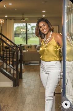 a woman in white pants and a gold top is standing by a glass door with her hands on her hips