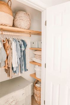 an open closet with baskets and clothes hanging on the shelves, next to a white door