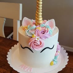 a white cake decorated with flowers and a unicorn's horn on top is sitting on a wooden table