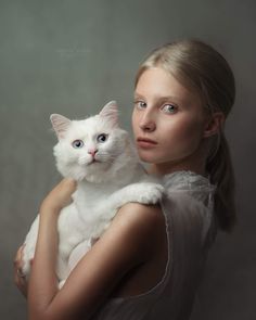 a woman is holding a white cat in her arms and looking at the camera with an intense look on her face