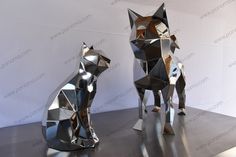 two metal foxes sitting next to each other on top of a silver surface with white wall in the background