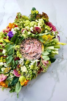 an arrangement of flowers and vegetables with a dip in the center on a marble surface