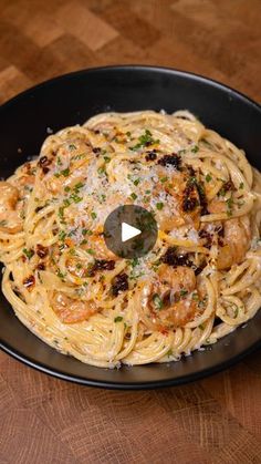 pasta with shrimp and parmesan cheese in a black bowl on a wooden table