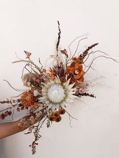 a woman holding a bouquet of flowers in her hand with white wall and background behind it