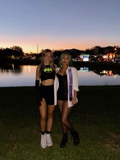 two women standing next to each other in front of a body of water at night