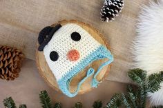 a crocheted snowman hat sitting on top of a piece of wood next to pine cones