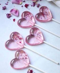 four heart shaped lollipops sitting on top of a white table next to pink flowers