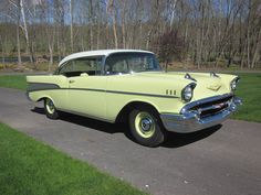 an old yellow car is parked on the side of the road in front of some trees