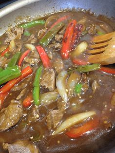 meat and vegetables are being cooked in a wok with a wooden spoon on the side