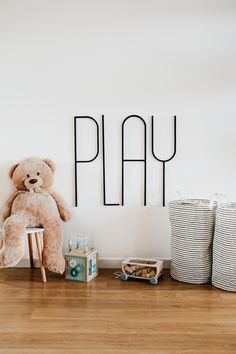 a teddy bear sitting on top of a wooden floor next to two baskets and a sign that says play