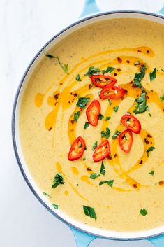 a pan filled with yellow soup and topped with sliced red tomatoes, green leaves and cheese