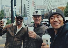 three men standing next to each other while holding up coffee cups in their hands and smiling at the camera