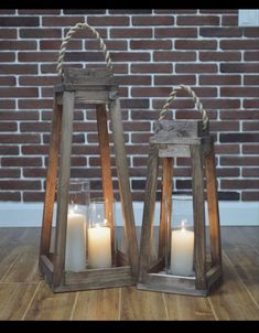 two wooden lanterns with white candles in them on a wood floor next to a brick wall