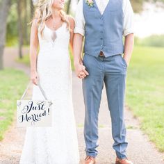 a bride and groom holding hands while standing on a path in the grass with a sign that says just married