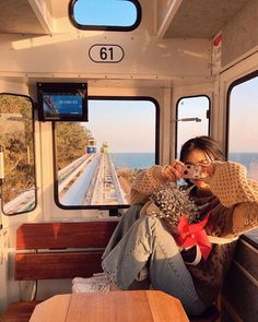 a woman sitting on a train looking out the window while holding up her cell phone