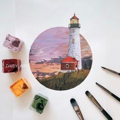 a painting of a lighthouse surrounded by paintbrushes and other art supplies on a white surface