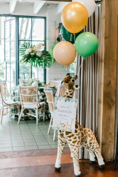 a giraffe holding onto some balloons in a room